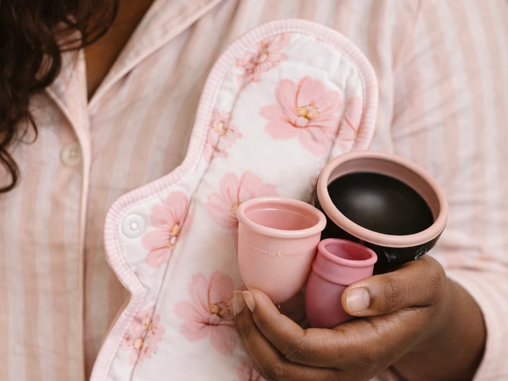 Reusable cloth pad and menstrual cups held against a soft pink blouse